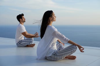 young couple practicing yoga at sunset in modern home terace with ocean and sunset in background